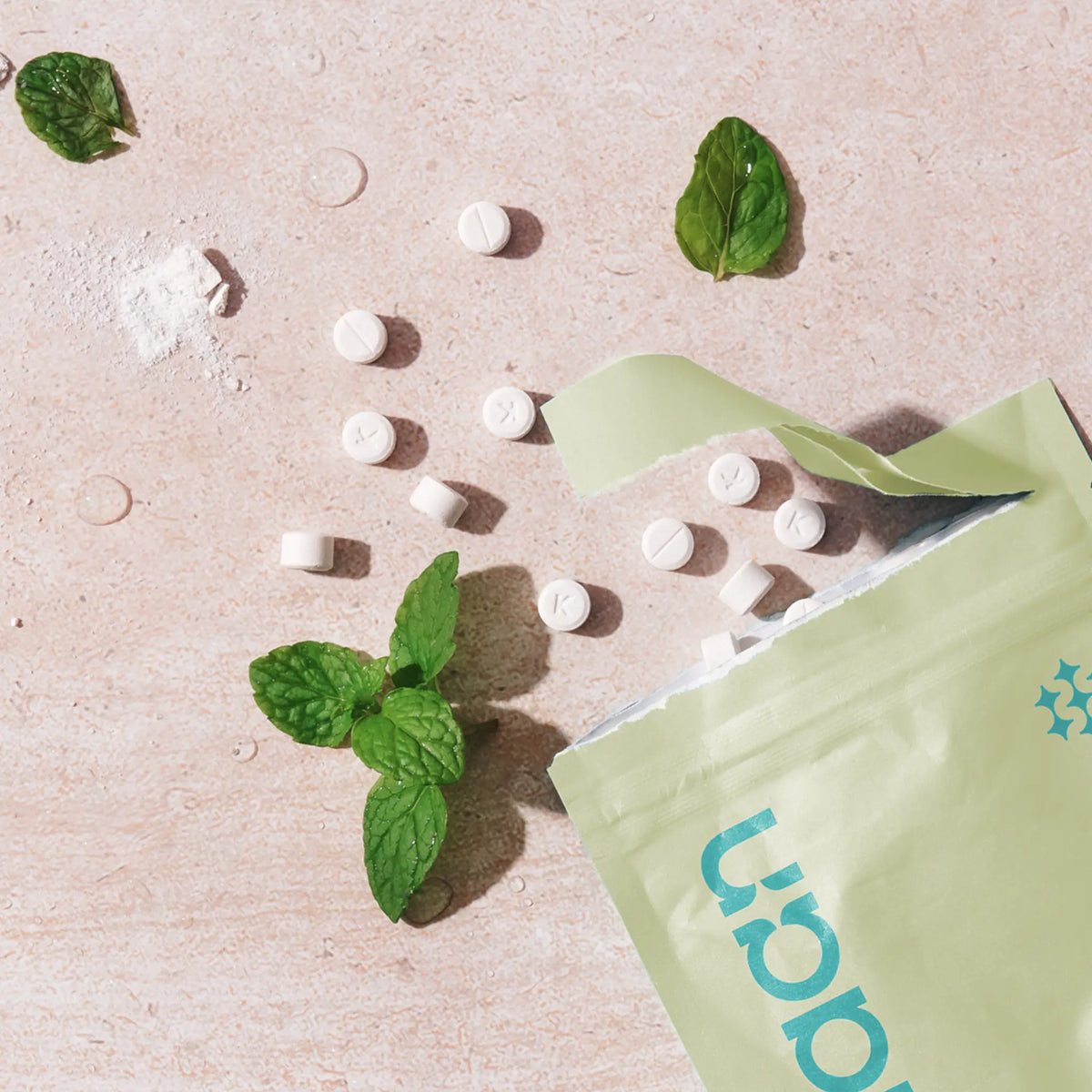 An open light green pouch of Kaylaan Organic Mint mouthwash tablets showing scattered white tabs and fresh mint leaves.